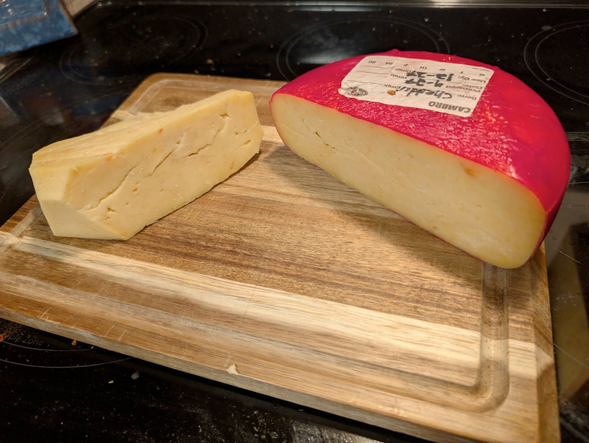 Homemade cheddar cheese wheel with red wax coating on a cutting board