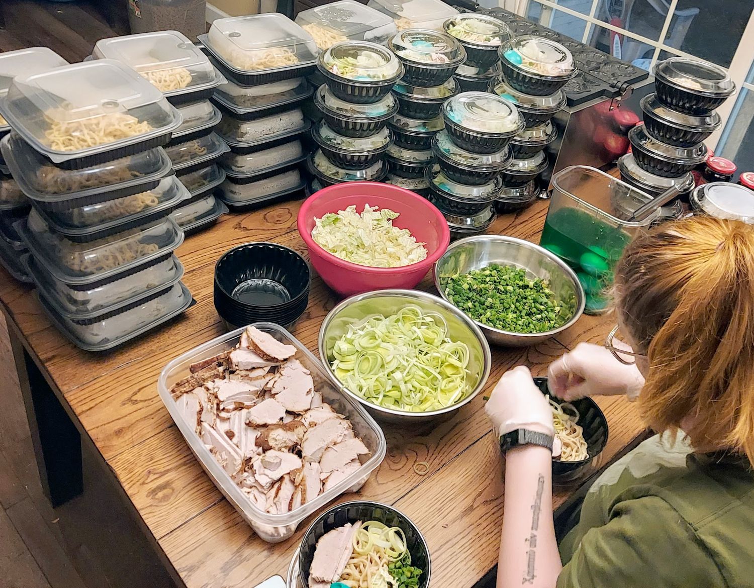 Bulk ramen prep — dozens of containers with chashu, noodles, leeks, and green onion