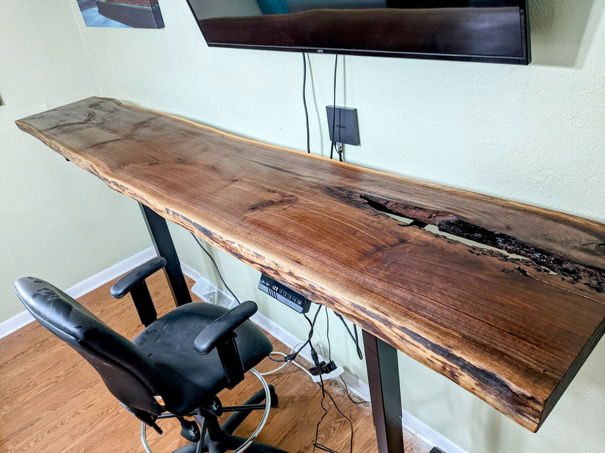 Live-edge walnut standing desk with dark epoxy fill on a motorized frame